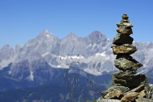 Man sieht einen gestapelten Haufen Steine vor der Bergkulisse des Dachstein - Massivs. Es ist ein strahlend schöner, wolkenloser Tag.